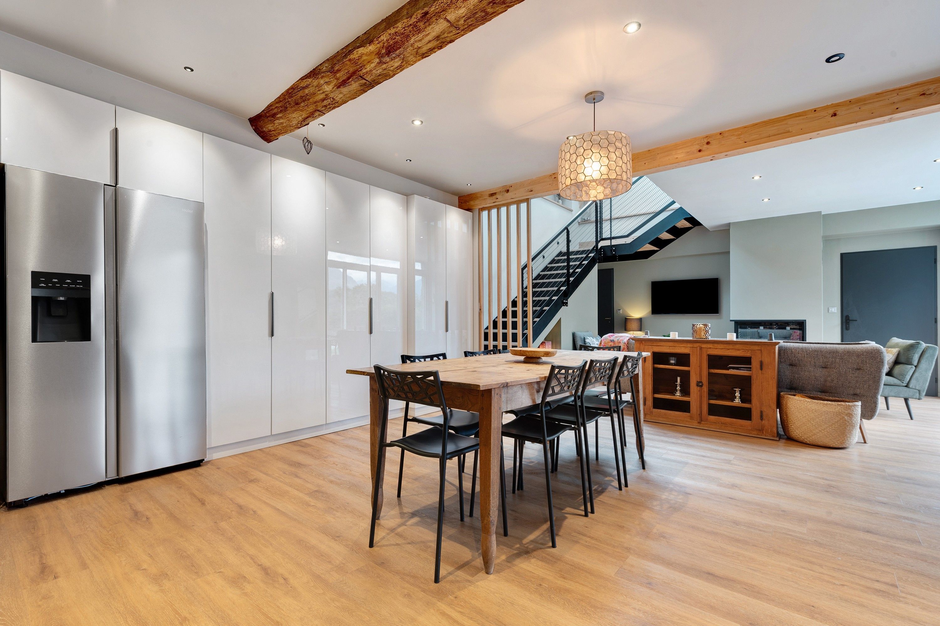 Une cuisine moderne avec des meubles blancs, une table à manger en bois et un escalier menant à l’étage supérieur.