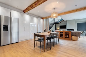 A modern kitchen with white cabinets, a wooden dining table, and a staircase leading to an upper level.