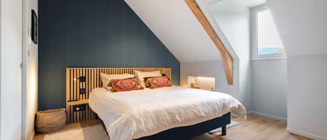 A bedroom with a sloped ceiling, a bed with white bedding, a wooden headboard, and a large window.