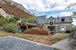 A stone house with a sloped roof, a covered porch, and a stone fireplace.