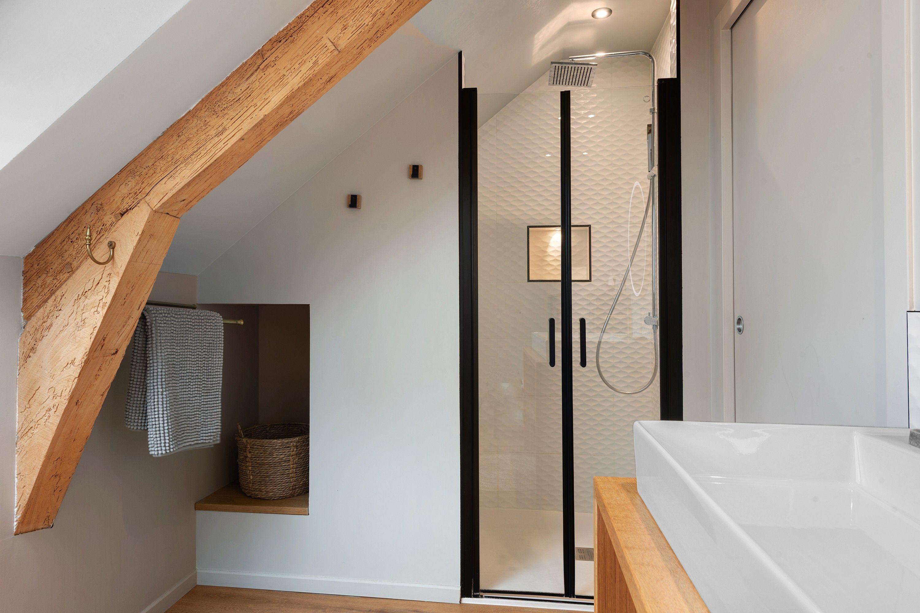 Ein modernes Badezimmer mit einer begehbaren Glasdusche, einem Holzbalken an der Decke, einer weißen Badewanne und einem Handtuchhalter.