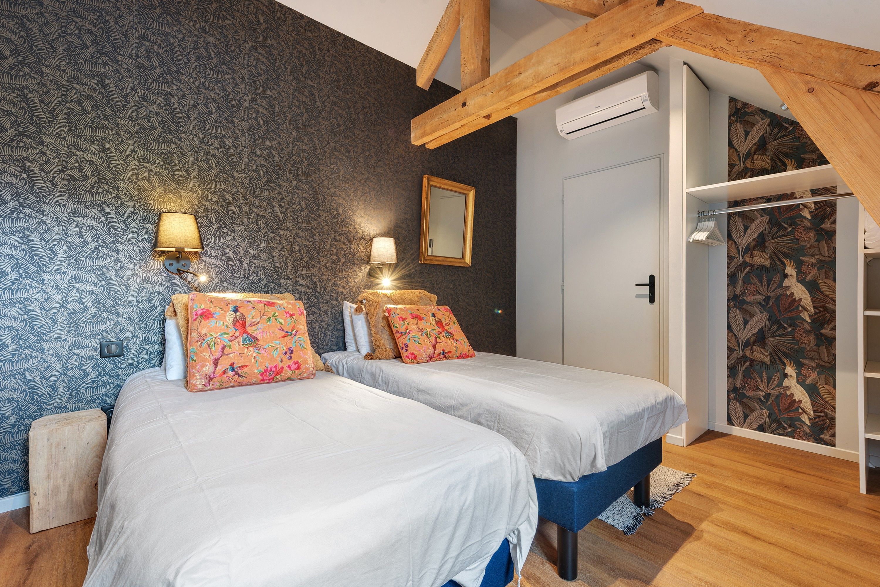 Une chambre avec deux lits, un plafond en bois, un appareil de climatisation et une armoire ornée d’un motif de feuilles tropicales.