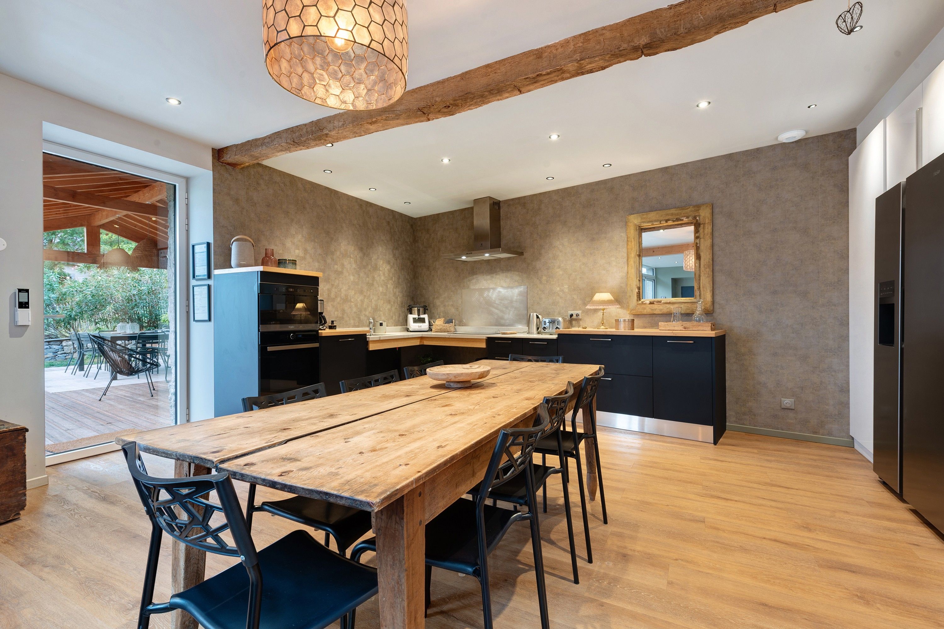 Una cocina moderna con una mesa de comedor de madera, sillas negras y un espejo grande sobre la encimera.