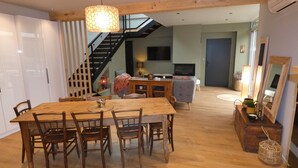 A spacious living area with a wooden dining table, chairs, a staircase, and a television. - Holiday Home “L’Escale Pibeste” with Mountain View, Wi-Fi and Air Conditioning (Agos-Vidalos)