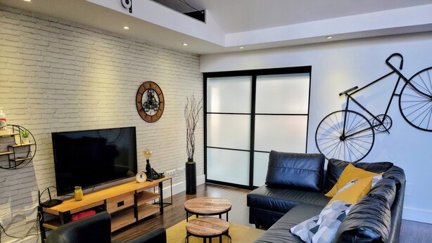 Un soggiorno moderno con una TV a schermo piatto, un divano in pelle, un tavolino da caffè e una bicicletta decorativa fissata al muro.