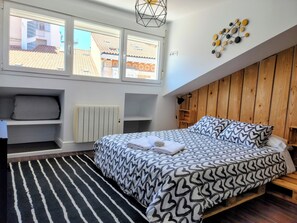 Ein Schlafzimmer mit einem Bett, einem Heizkörper, einem Fenster, einer Holzwand und einer Wandleuchte.