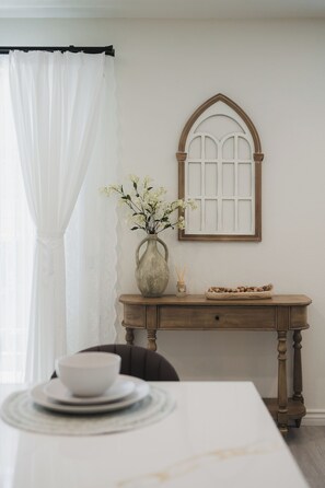 Un coin repas avec une table dressée pour deux personnes, un vase rempli de fleurs, une console en bois et un miroir décoratif.