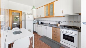 A compact kitchen with white cabinets, a stove, a microwave, and a dining table with chairs. - GuestReady - Charming retreat with balcony in Gaia (Vila Nova de Gaia)