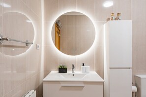 A modern bathroom with a round mirror, white sink, and a toilet. - GuestReady - Charming retreat with balcony in Gaia (Vila Nova de Gaia)
