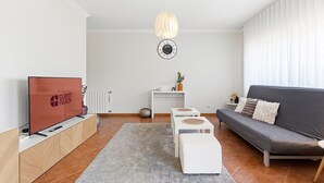 A modern living room with a flat-screen TV, a sofa, a coffee table, a rug, and a pendant light. - GuestReady - Charming retreat with balcony in Gaia (Vila Nova de Gaia)