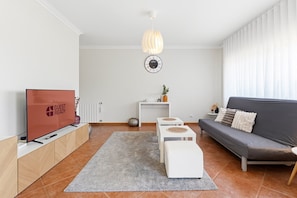 Ein modernes Wohnzimmer mit Flachbildfernseher, einer Couch, einem Couchtisch, einem Teppich und einer Pendelleuchte.