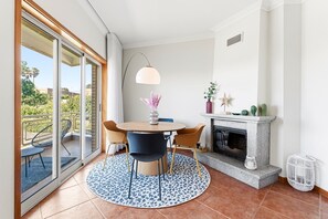 A room with a round table, chairs, a fireplace, a balcony with chairs, and a view of greenery. - GuestReady - Charming retreat with balcony in Gaia (Vila Nova de Gaia)