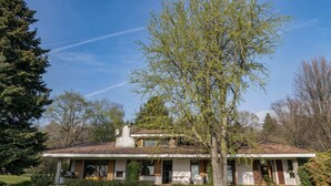 Une maison à deux étages dotée d’un porche abrité, entourée d’une pelouse bien entretenue et d’arbres.