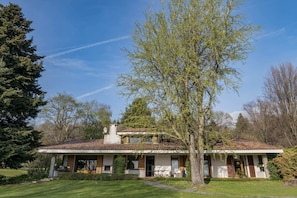 Una casa a due piani con un portico coperto, circondata da un prato curato e alberi.