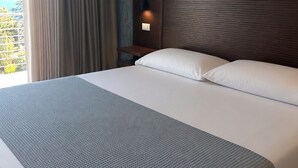 A hotel room with a large bed, a nightstand with a lamp, a window with curtains, and a wall with a bamboo pattern. - Marèa - Capo Vaticano (Ricadi)