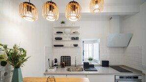 Eine moderne Küche mit weißen Schränken, einem Holztisch und einem Einbauofen, beleuchtet von Pendelleuchten.