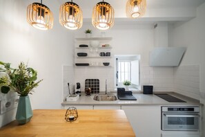 Eine moderne Küche mit weißen Schränken, einem Holztisch und einem Einbauofen, beleuchtet von Pendelleuchten.