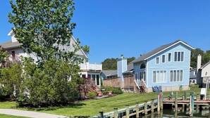 A residential area with a grassy lawn, a wooden dock, and houses with blue siding. - WATERFRONT HOME  Ocean Pines Dog Friendly (Ocean Pines)