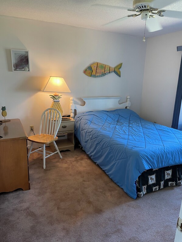 A bedroom with a bed, a desk, a chair, a lamp, a ceiling fan, and a fish decoration on the wall.