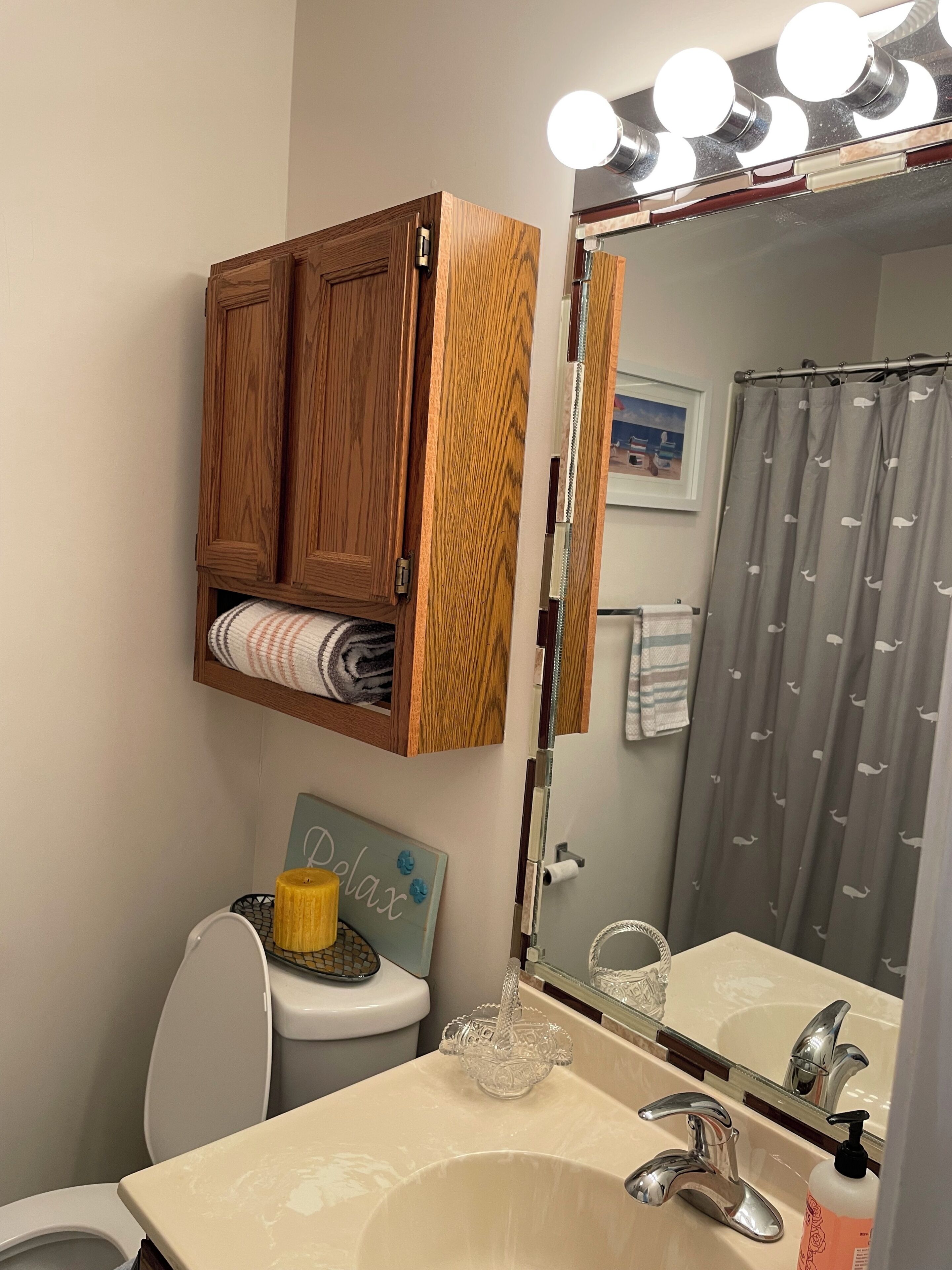 A bathroom with a wooden cabinet above the toilet, a sink with a mirror, and a shower curtain.