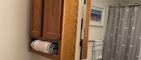 A bathroom with a wooden cabinet above the toilet, a sink with a mirror, and a shower curtain.