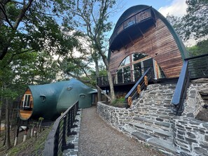 A wooden cabin with a curved roof and a staircase leading to a deck. - Oscar winning living @ Livingstations (Woodstock)