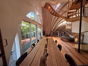 A spacious room with a long wooden table, multiple chairs, a staircase, and large windows offering a view of the outdoors. - Oscar winning living @ Livingstations (Woodstock)