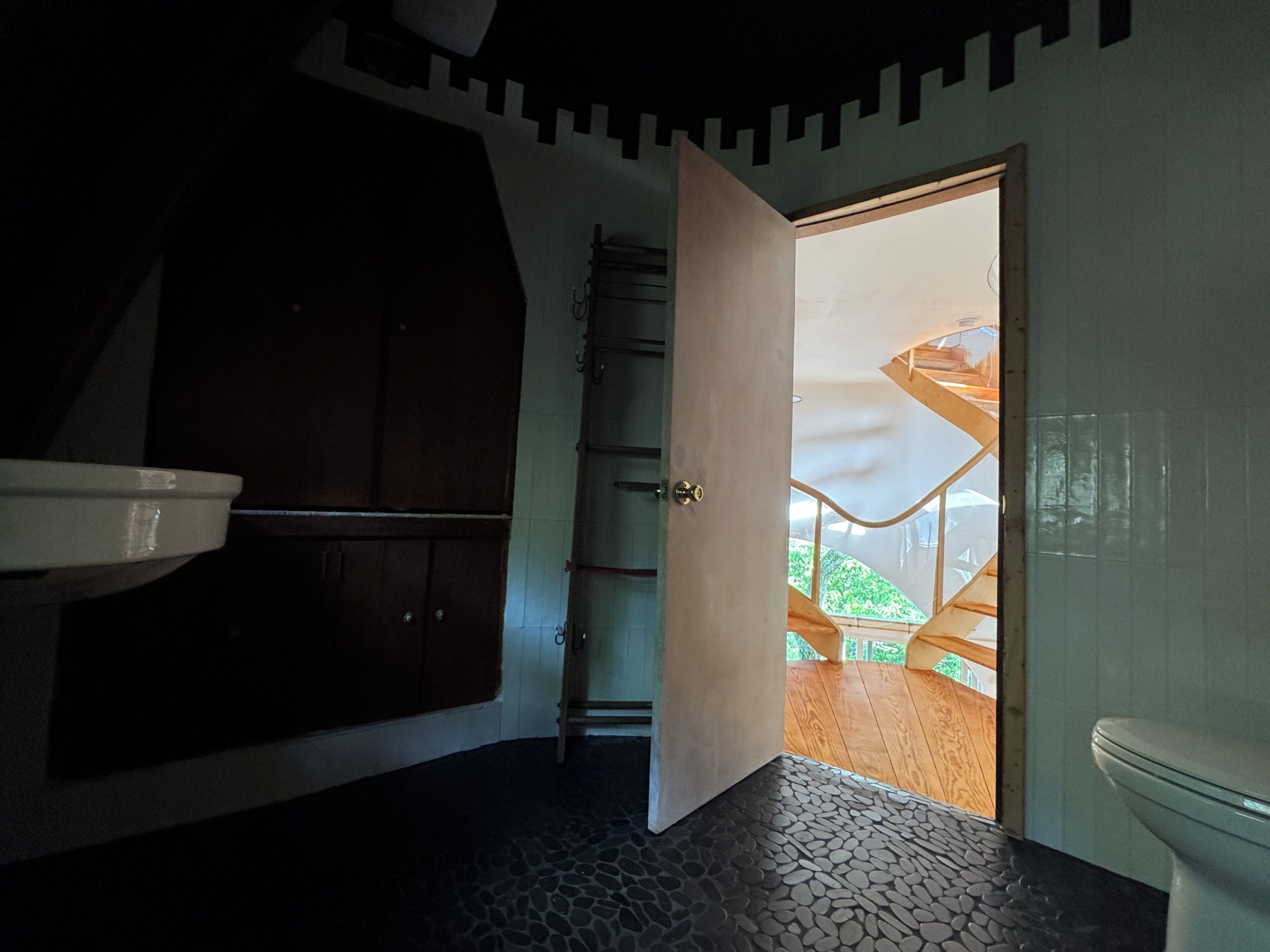 Un baño con un lavamanos blanco, un inodoro, una puerta de madera que da a un balcón y un suelo con estampado.