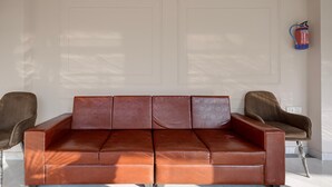 A brown leather sofa with a matching armchair, a fire extinguisher on the wall, and a white door in the background. - Deluxe With Balcony Haldwani inn 2.0 (Haldwani)