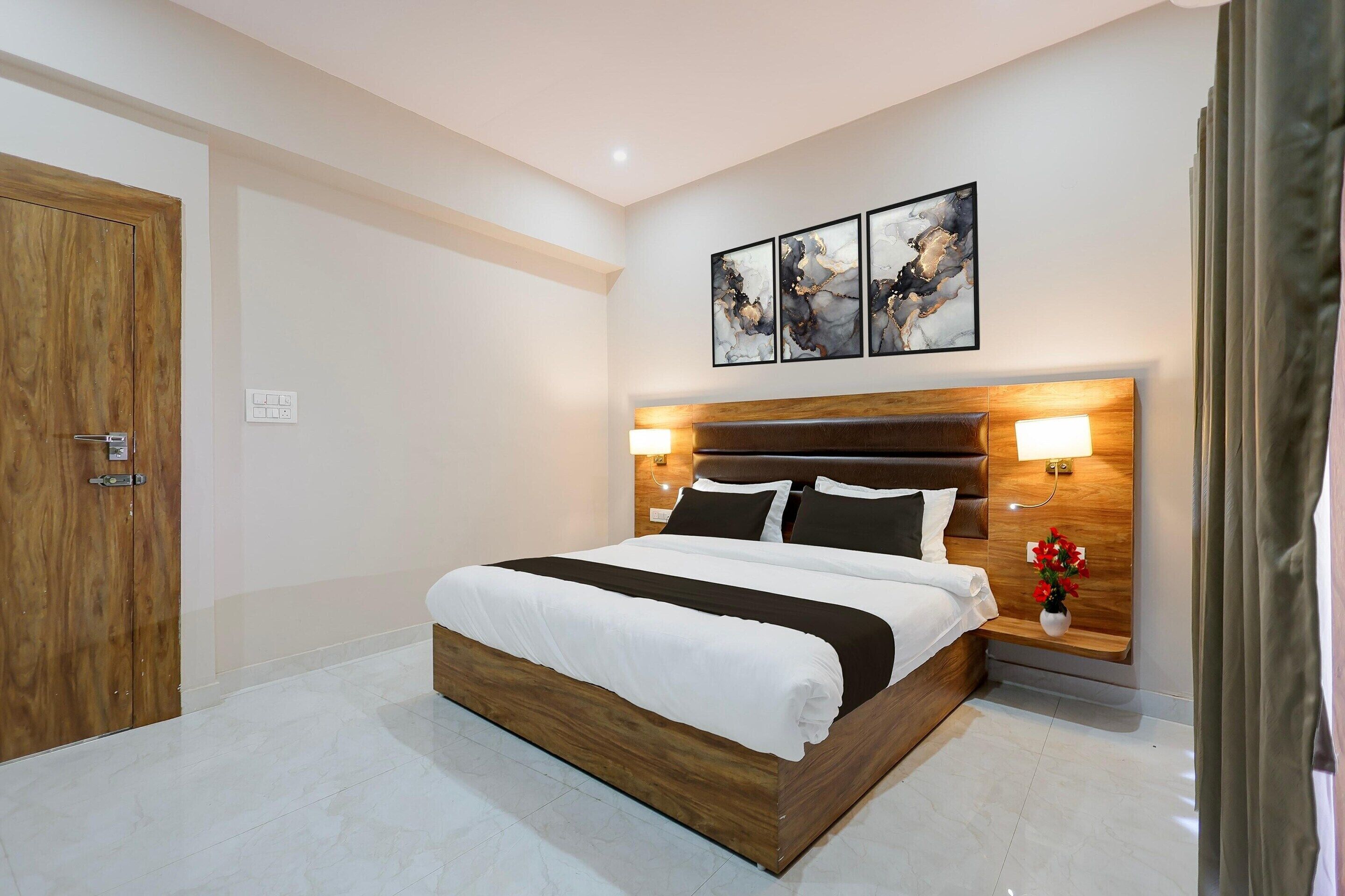 A modern hotel room with a wooden bed, a nightstand with a lamp, and a wall-mounted artwork above the bed.