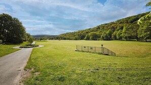A rural landscape with a paved path, grassy fields, and a fenced area. - Host & Stay | Lower Cross Lee Cottage (Todmorden)