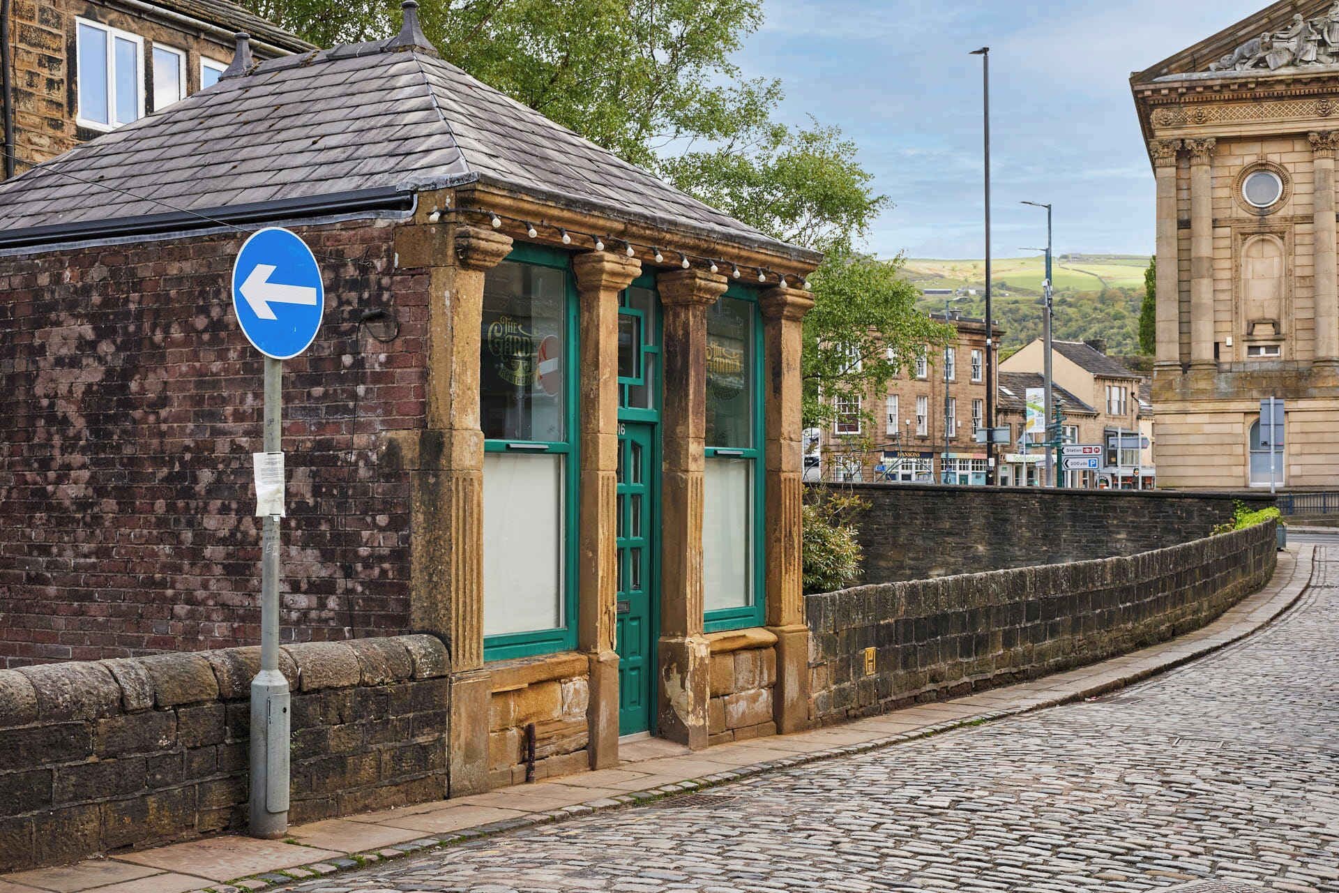 A historic building with a stone facade, a green door, and a blue directional sign.
