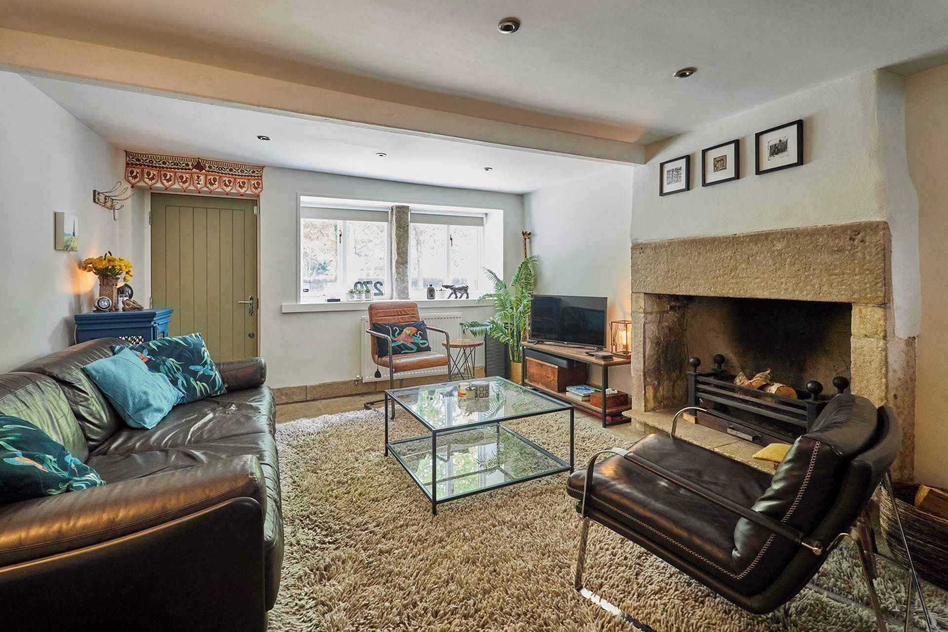 A living room with a fireplace, leather sofa, glass coffee table, and a television.
