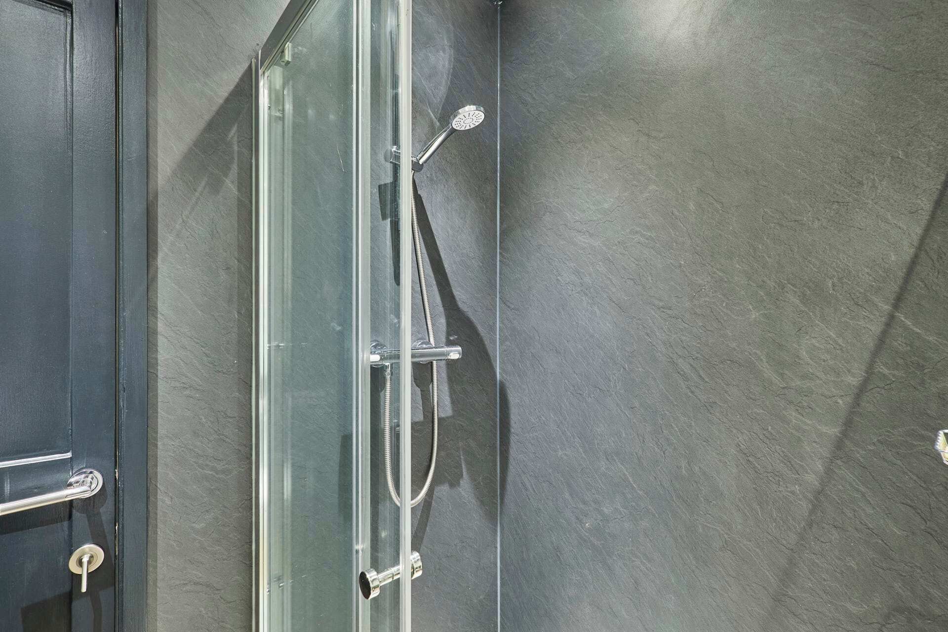 Une douche dotée d’une porte en verre et d’un flexible, installée devant un mur à texture.