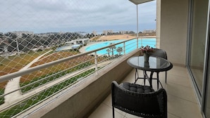 A balcony with a view of a swimming pool, a table with chairs, and a railing. - Oceana Suites Laguna Bahía (Algarrobo)