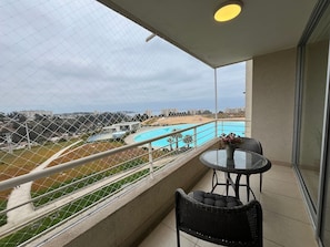 Un balcon donnant sur une piscine, une table avec des chaises et une rambarde.