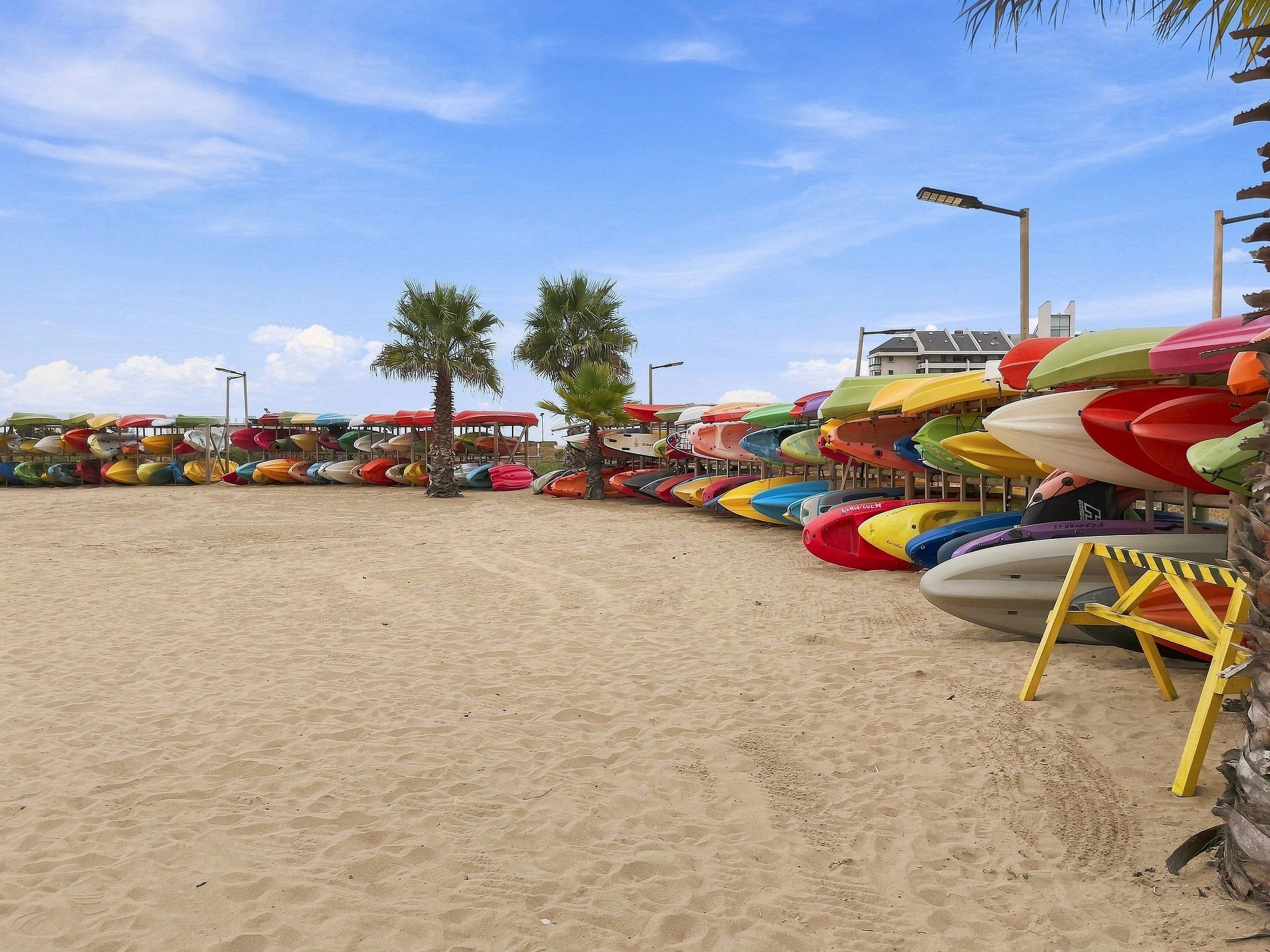 A beach with rows of colorful kayaks and a yellow lifeguard stand.