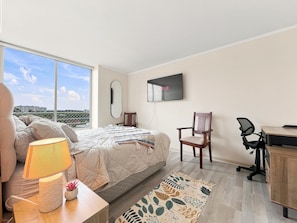 Une chambre avec un lit, un bureau, une chaise, une télévision et une vue sur la ville.
