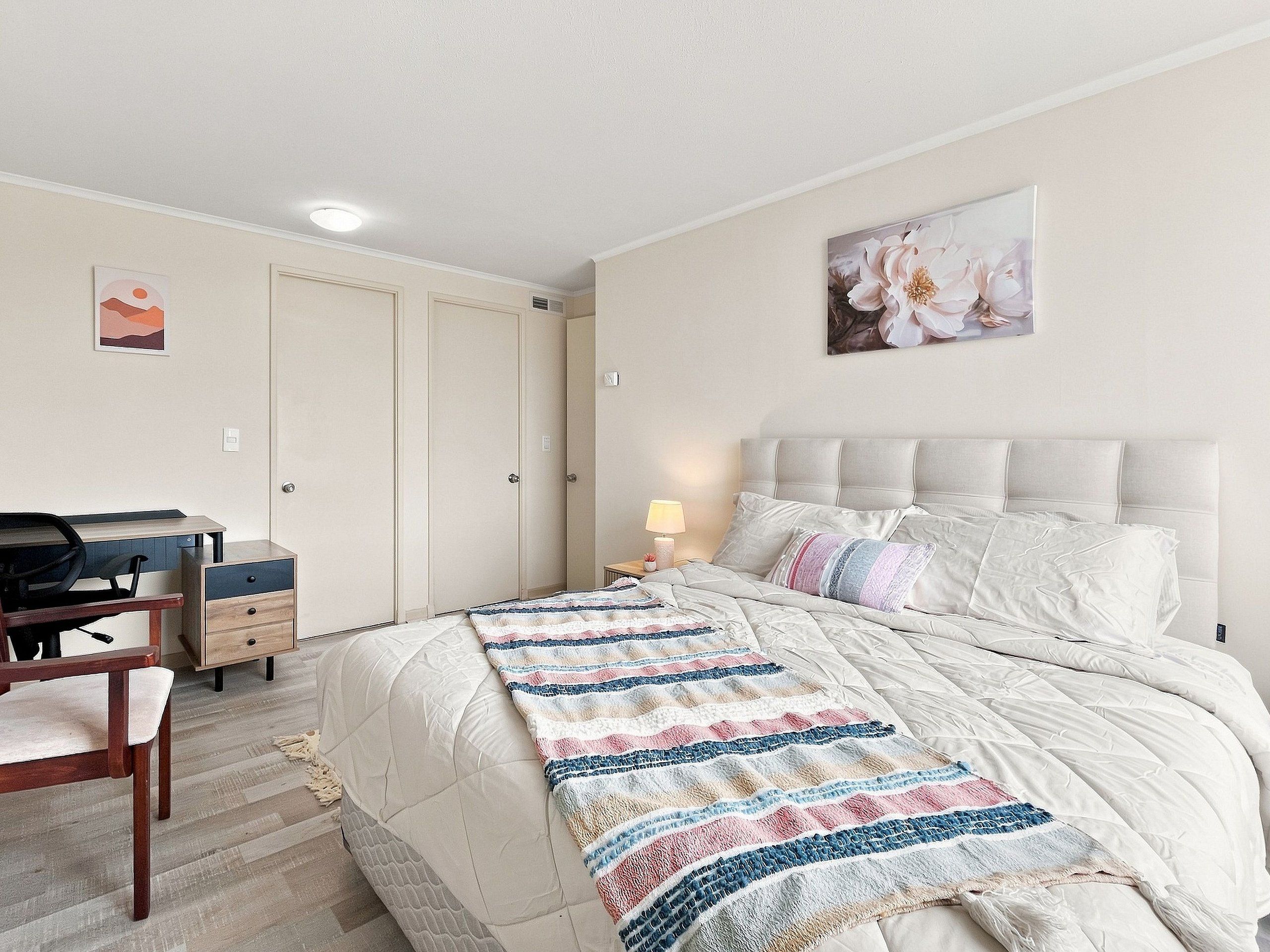 Un dormitorio con cama, escritorio y silla. Se observa una puerta y una pared con un cuadro.