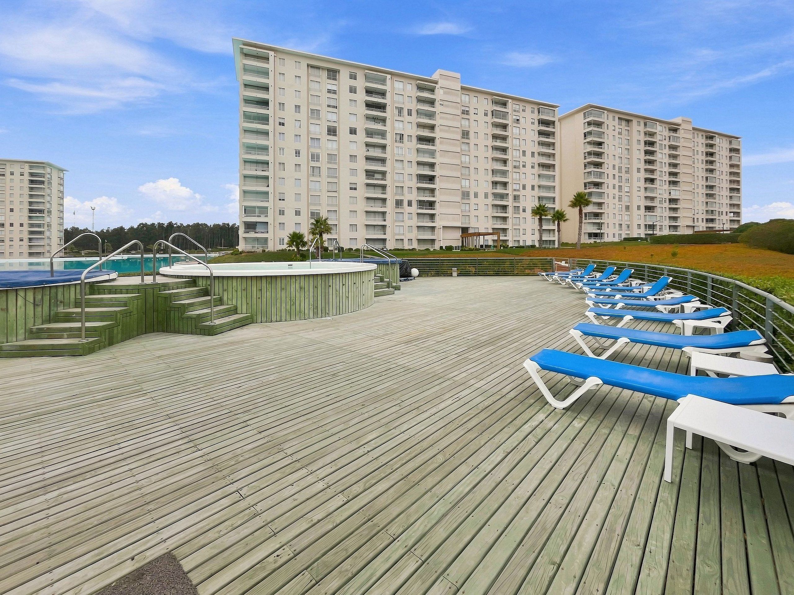A wooden deck with lounge chairs and a pool area, surrounded by high-rise buildings.