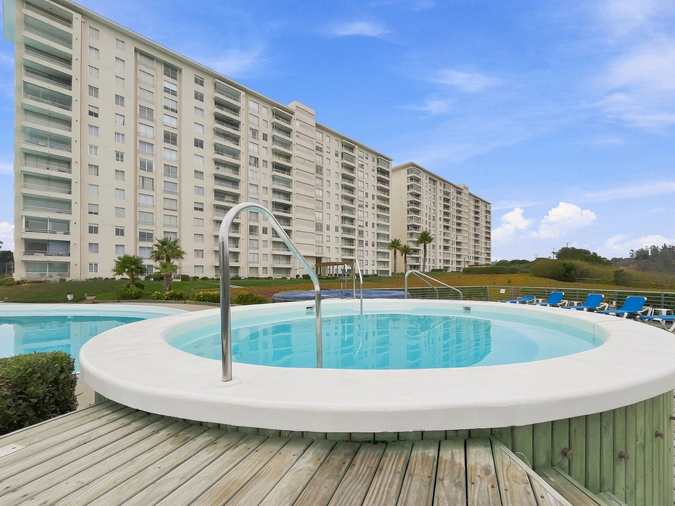 Ein Schwimmbad mit Holzdeck, umgeben von einem Hochhaus mit zahlreichen Balkonen.