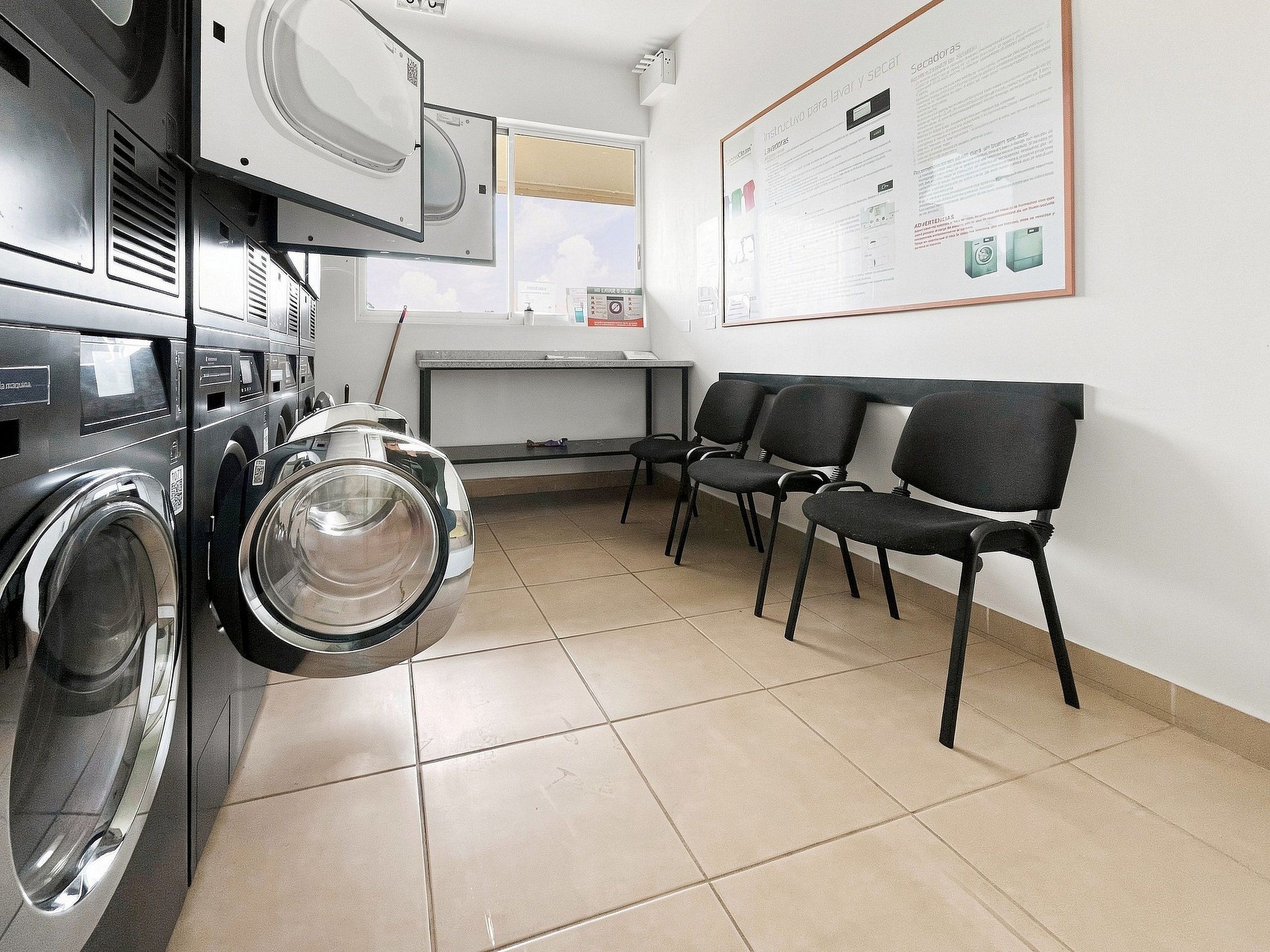 A laundry facility with multiple washing machines, a seating area with chairs, and a wall-mounted informational poster.