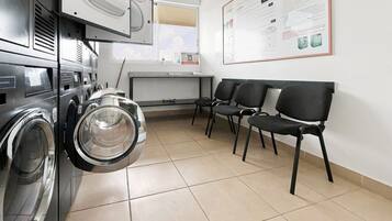 A laundry facility with multiple washing machines, a seating area with chairs, and a wall-mounted informational poster.