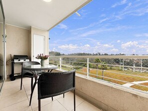 Un balcon avec un barbecue, des meubles en osier et une vue sur la campagne.