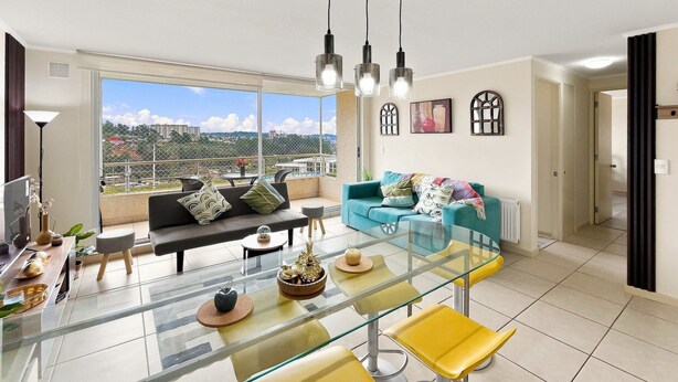 A modern living room with a glass dining table, a sofa, and a view of the cityscape. - Oceana Suites Laguna Bahía (Algarrobo)