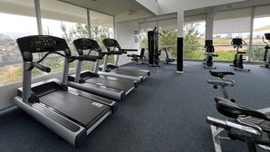A gym with treadmills, exercise bikes, and weight machines, large windows, and a view of greenery. - Oceana Suites Laguna Bahía (Algarrobo)