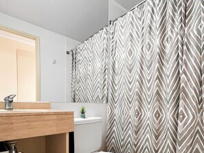Une salle de bain avec un meuble-lavabo en bois, des toilettes et un rideau de douche à motifs géométriques.