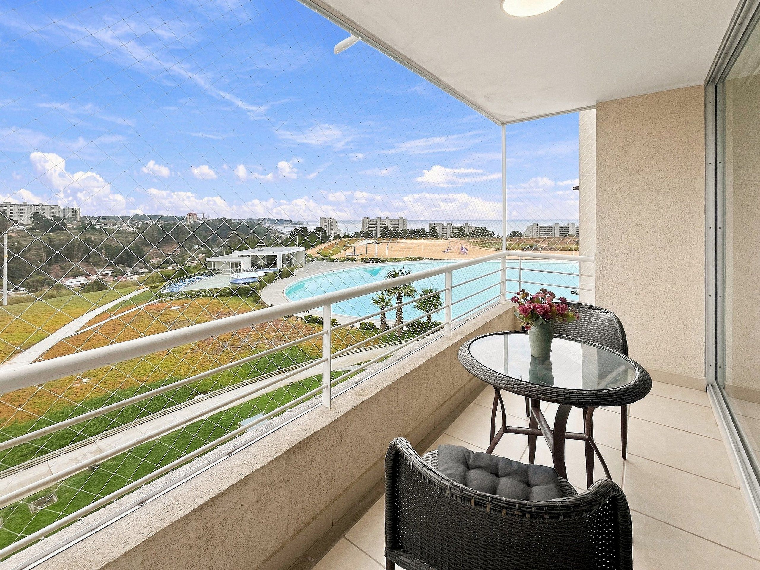 A balcony with a view of a swimming pool, a grassy area, and distant buildings.