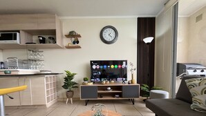 A modern living room with a TV, sofa, dining table, and kitchen area. - Oceana Suites Laguna Bahía (Algarrobo)