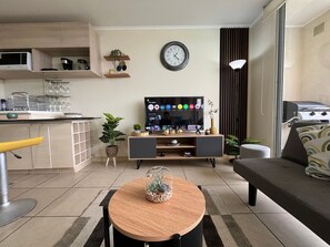 A modern living room with a TV, sofa, dining table, and kitchen area. - Oceana Suites Laguna Bahía (Algarrobo)